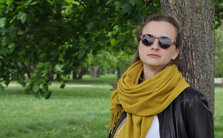 Ráchel Skleničková opřená o strom v parku.